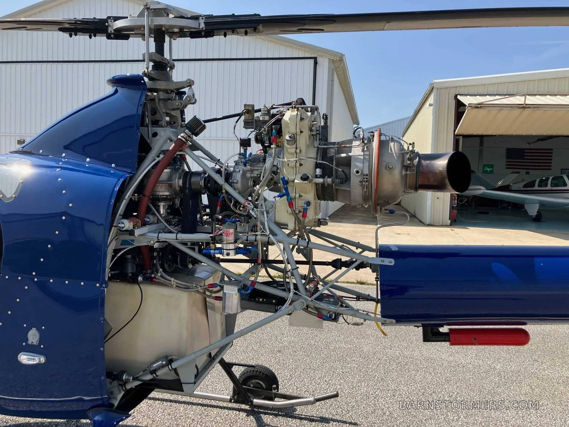 A close-up view of the exposed turbine engine and internal components of a blue helicopter with its cowling removed.