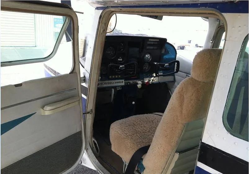 View into the cockpit and cabin of the Cessna Skylane N2342X with an open door and sheepskin seat cover.