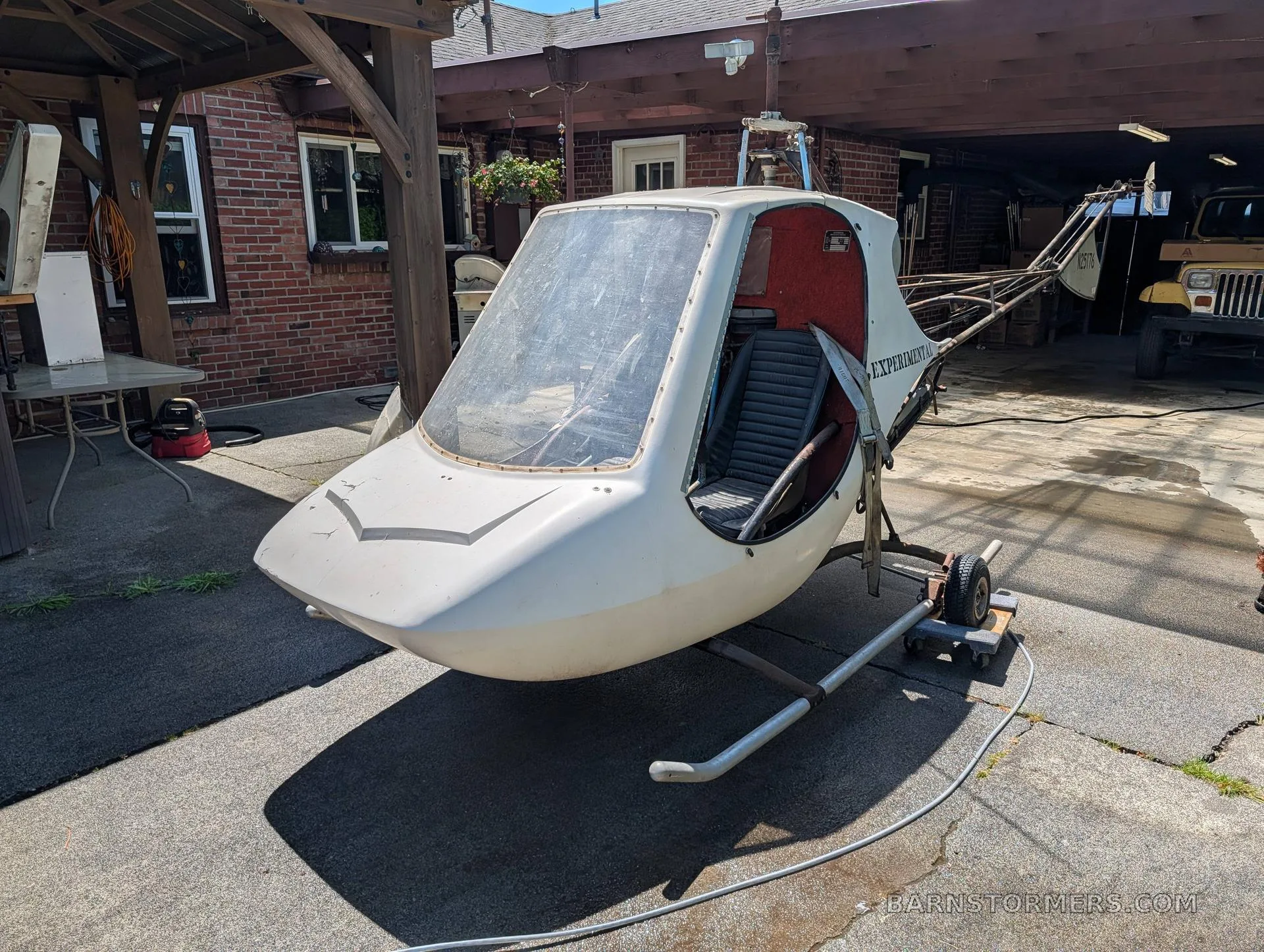 A white experimental Scorpion Too helicopter with an open cockpit, parked on a concrete driveway next to a brick building.