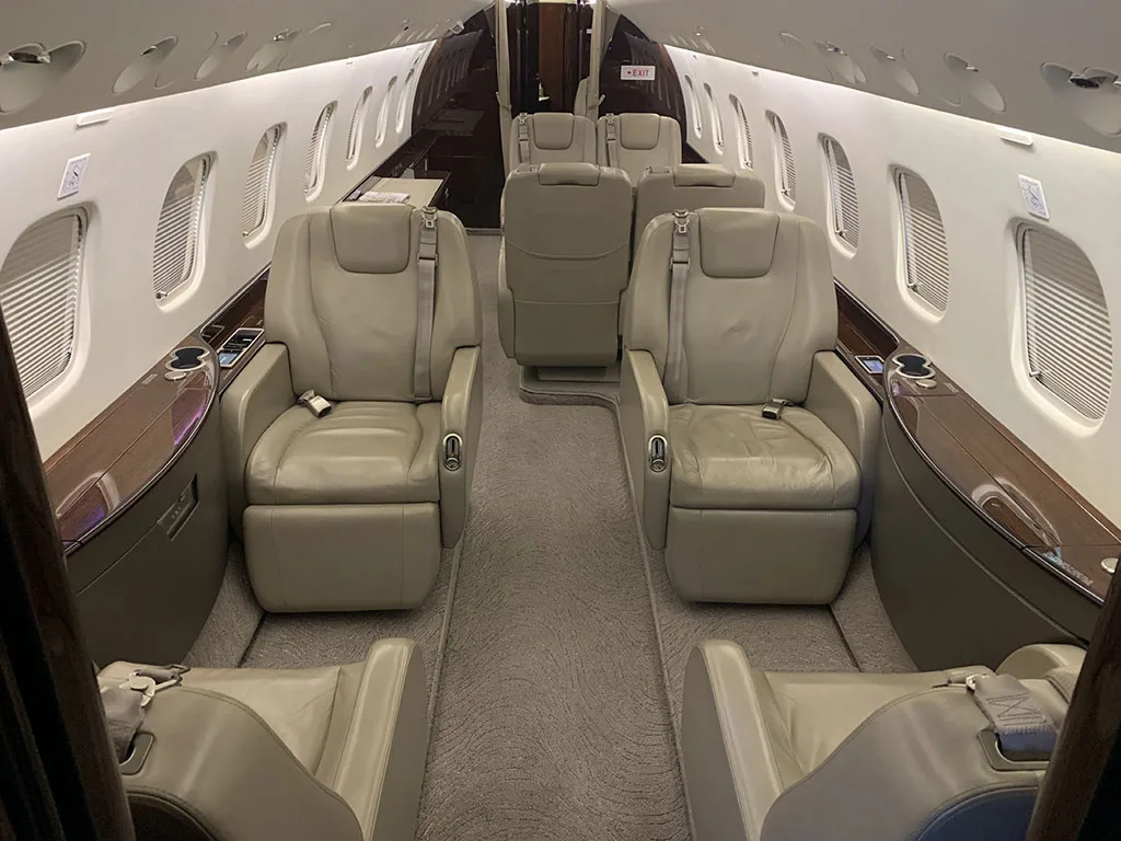 The luxurious cabin interior of the Embraer Legacy 650, featuring light beige leather seats and dark wood accents.