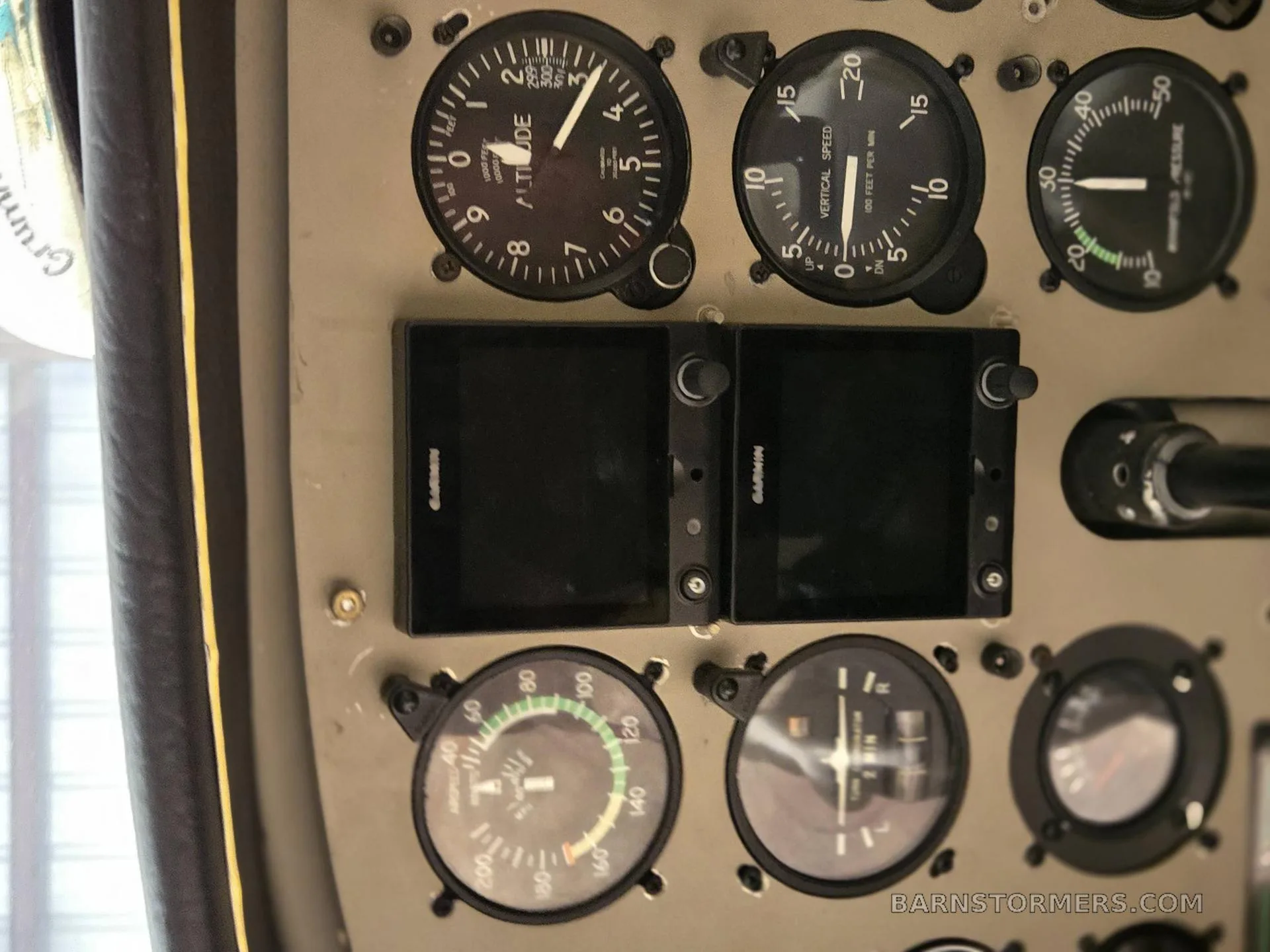 A close-up of the aircraft's instrument panel, highlighting the altitude, vertical speed gauges, and two Garmin displays.
