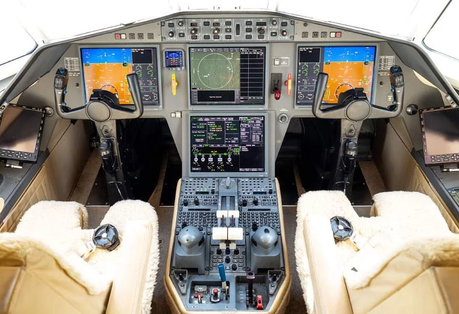 The modern cockpit of a business jet, featuring multiple digital displays and two pilot seats with sheepskin covers.
