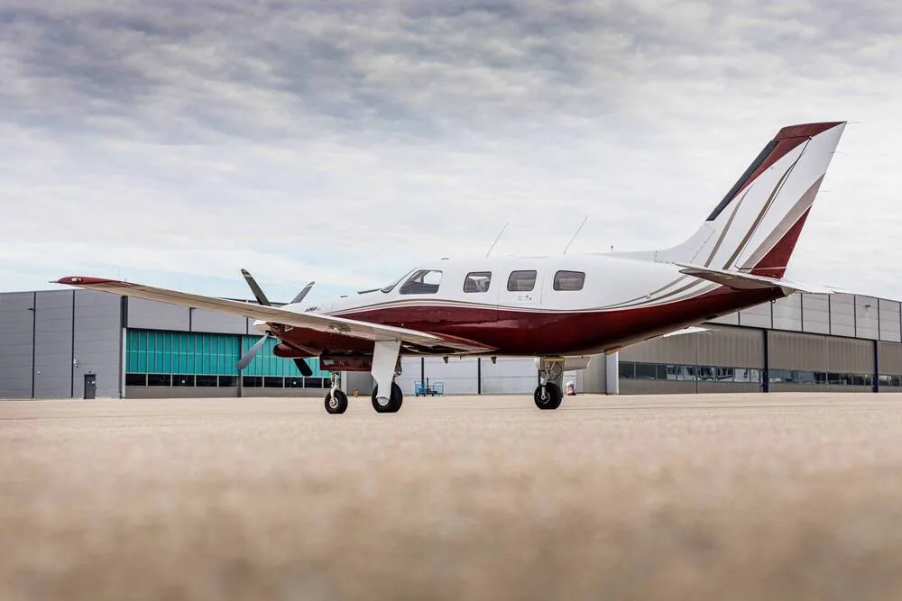 A white and maroon single-engine turboprop aircraft viewed from the rear-right, parked on an airfield.