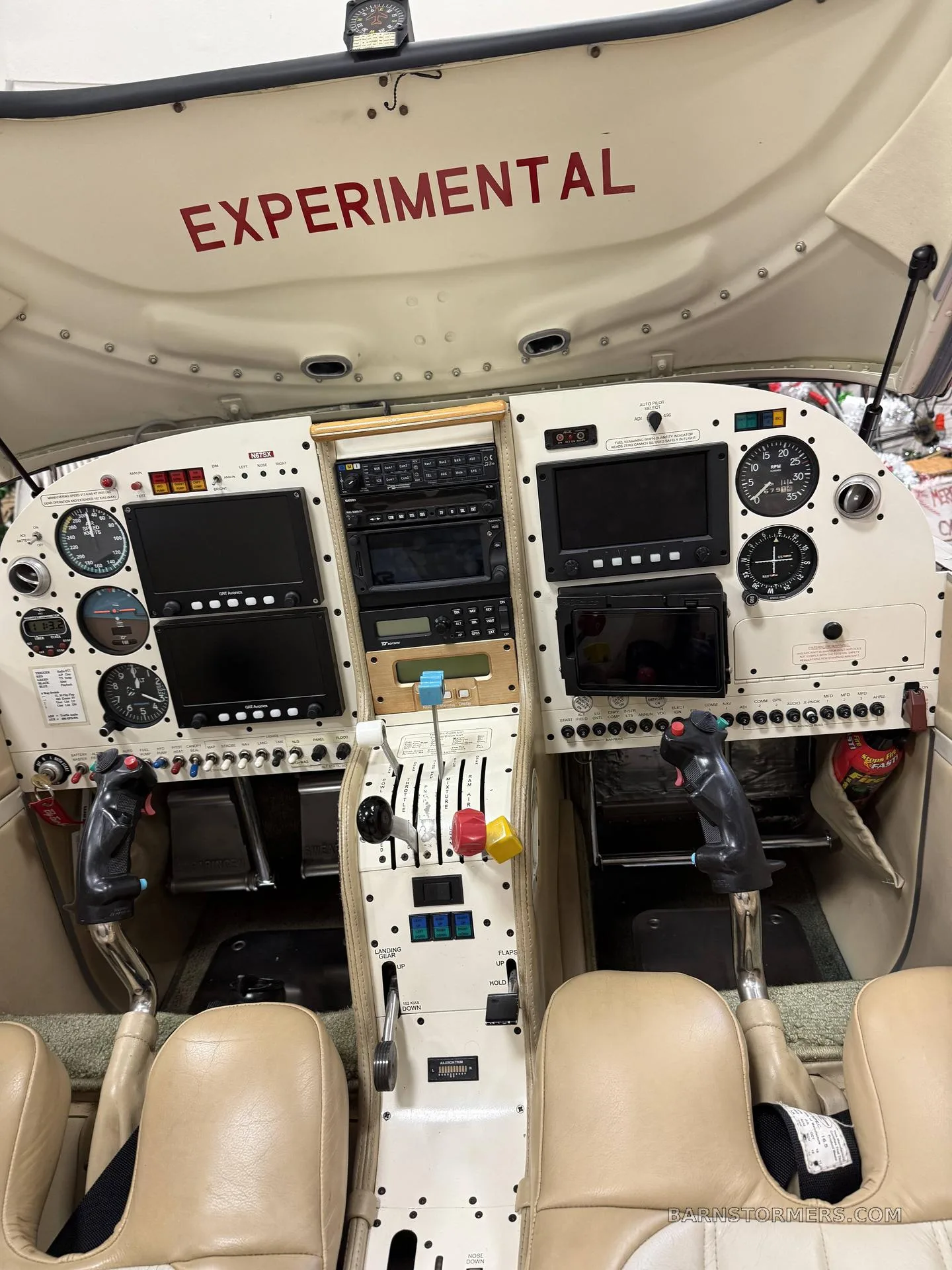 The cockpit of an experimental aircraft, showing the instrument panel with multiple screens, controls, and two light brown seats.