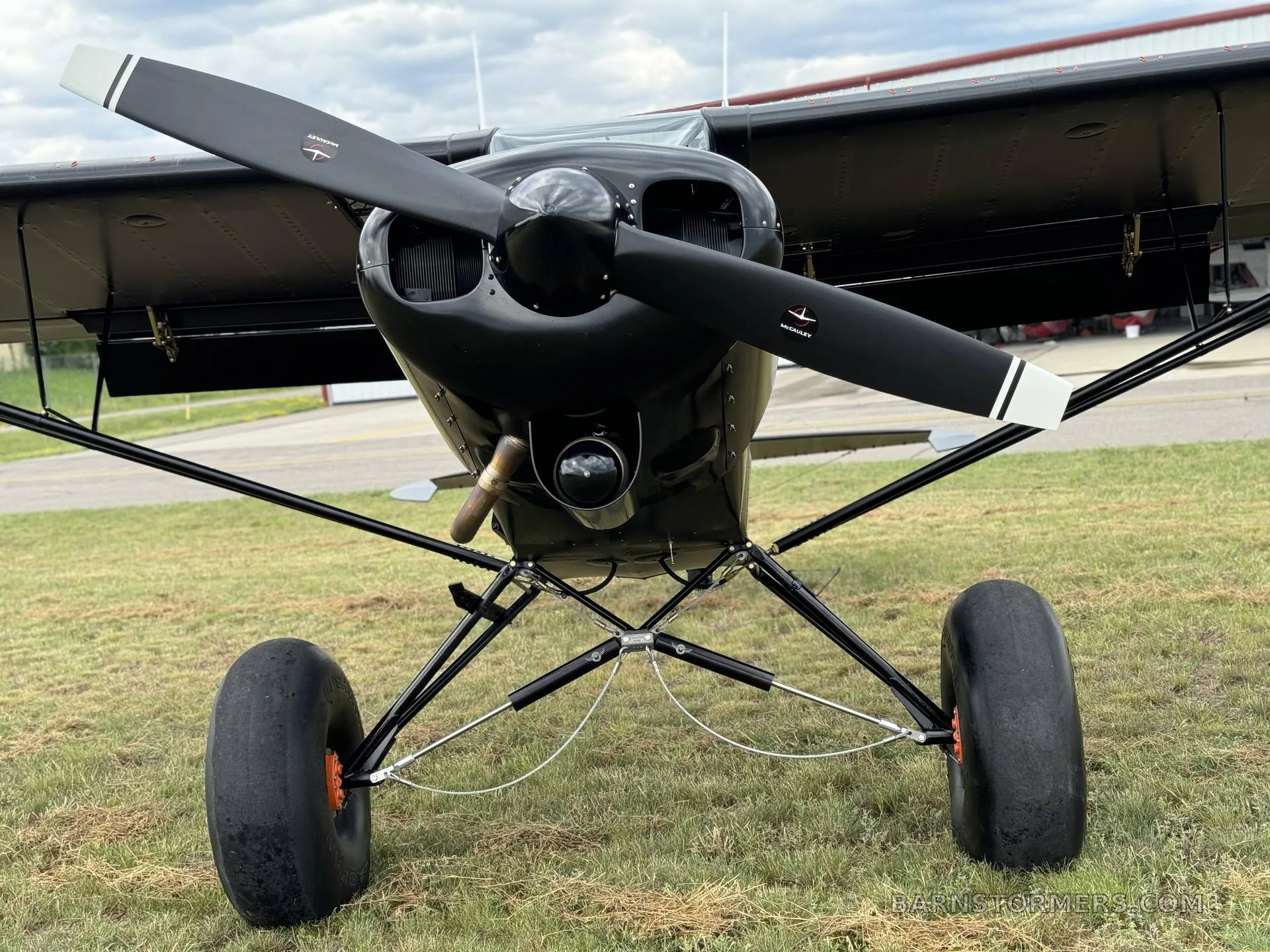 A black Super Cub 180 aircraft with a two-blade propeller and large bush wheels, viewed head-on on a grassy field.