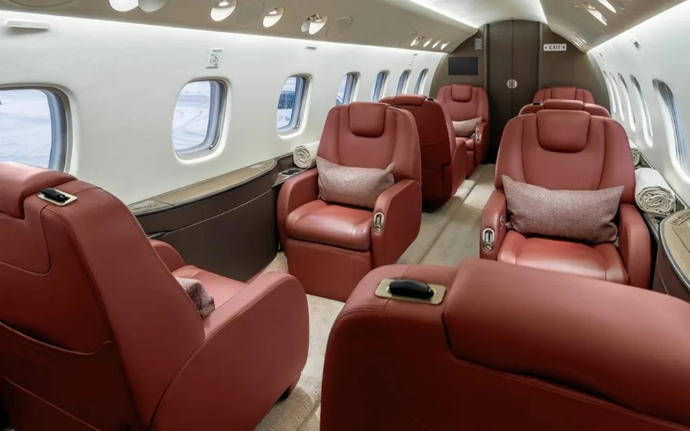 View of a luxurious aircraft cabin with multiple rows of red leather reclining seats and large windows.