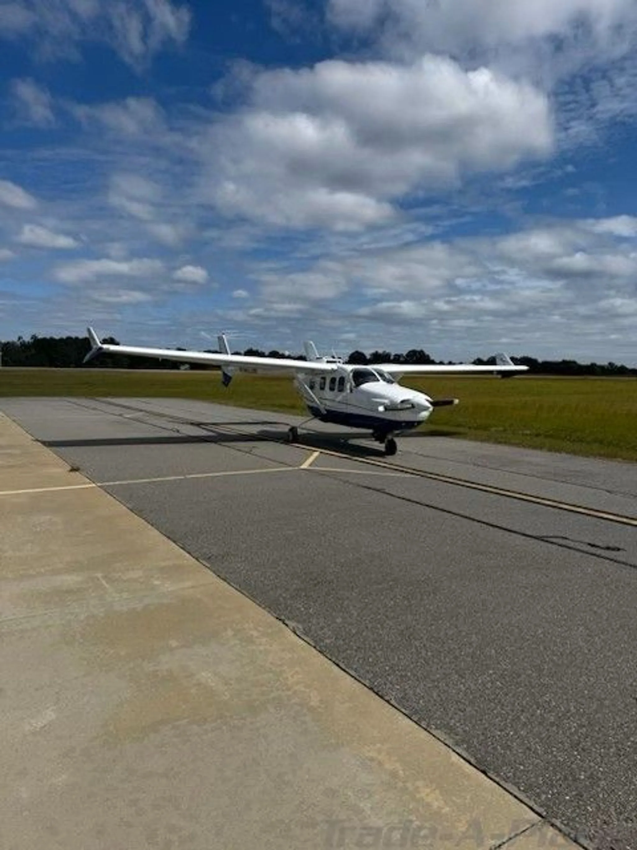 A white and blue Cessna 337 Skymaster aircraft on a tarmac under a partly cloudy sky.