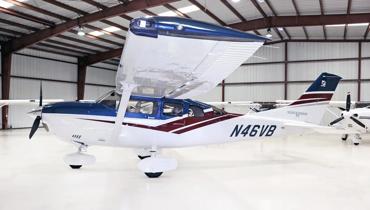 A white Cessna Stationair TC with blue and maroon stripes is parked in a hangar.