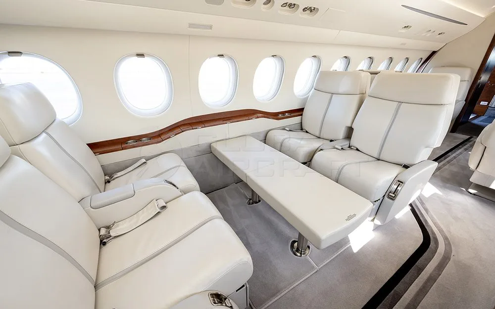 The interior of a private jet cabin with light leather seats and a convertible bench or bed along the side.