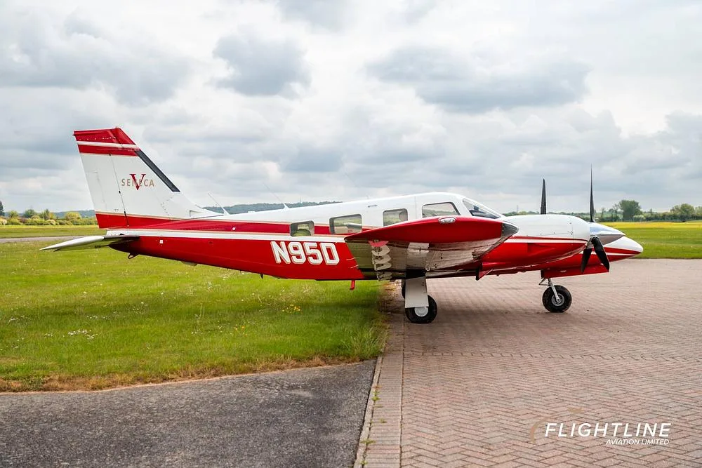 A red and white Piper Seneca aircraft with registration N95D parked on a paved surface, viewed from the left side.