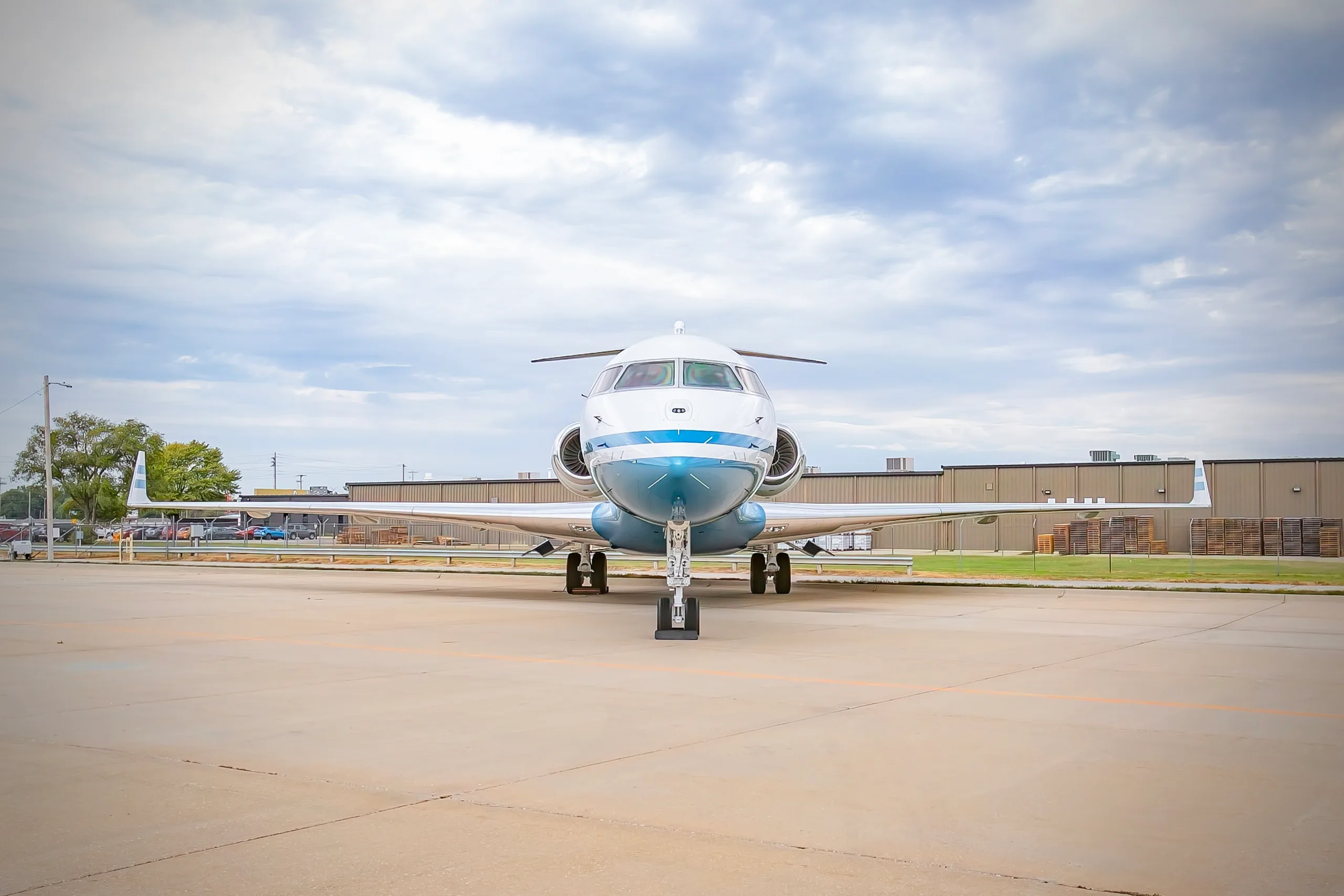 A head-on view of a white and blue business jet, likely a Bombardier Global, parked on an airport tarmac.