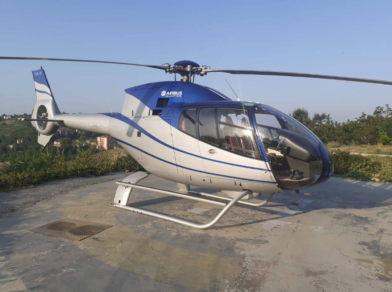 An Airbus H120 Colibri helicopter in blue and silver livery parked on an outdoor helipad.