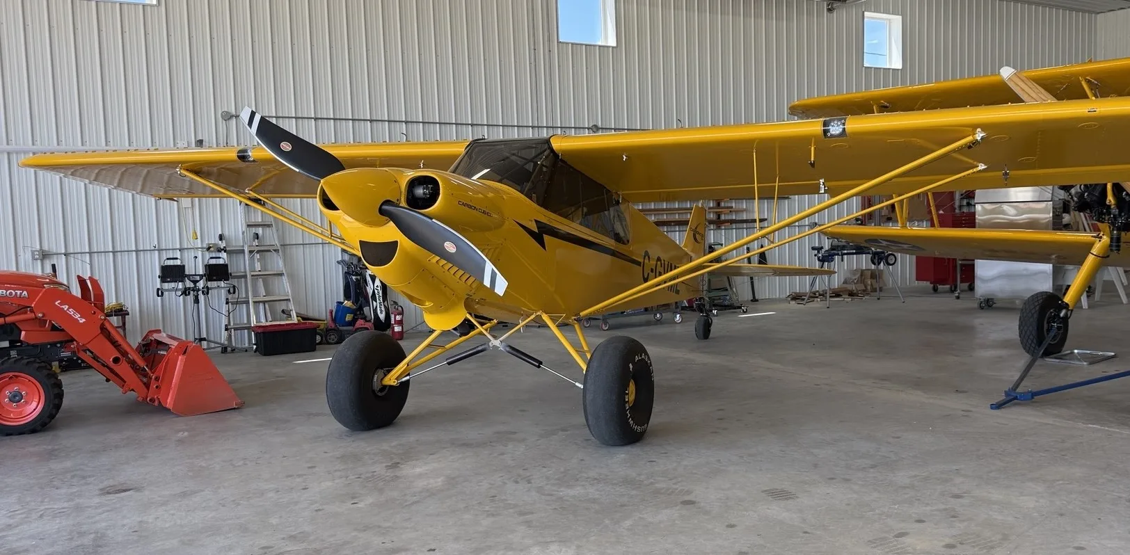 A yellow CubCrafters Carbon Cub EX-3 with large tires parked in a hangar, seen from the front-left.