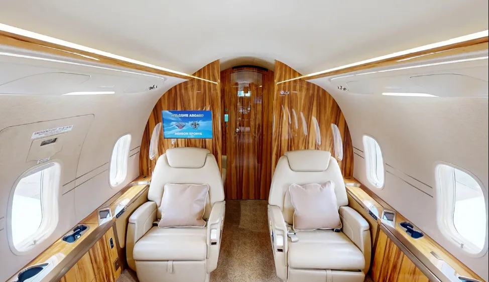 A section of a private jet's interior cabin featuring two light leather seats and polished wood paneling.