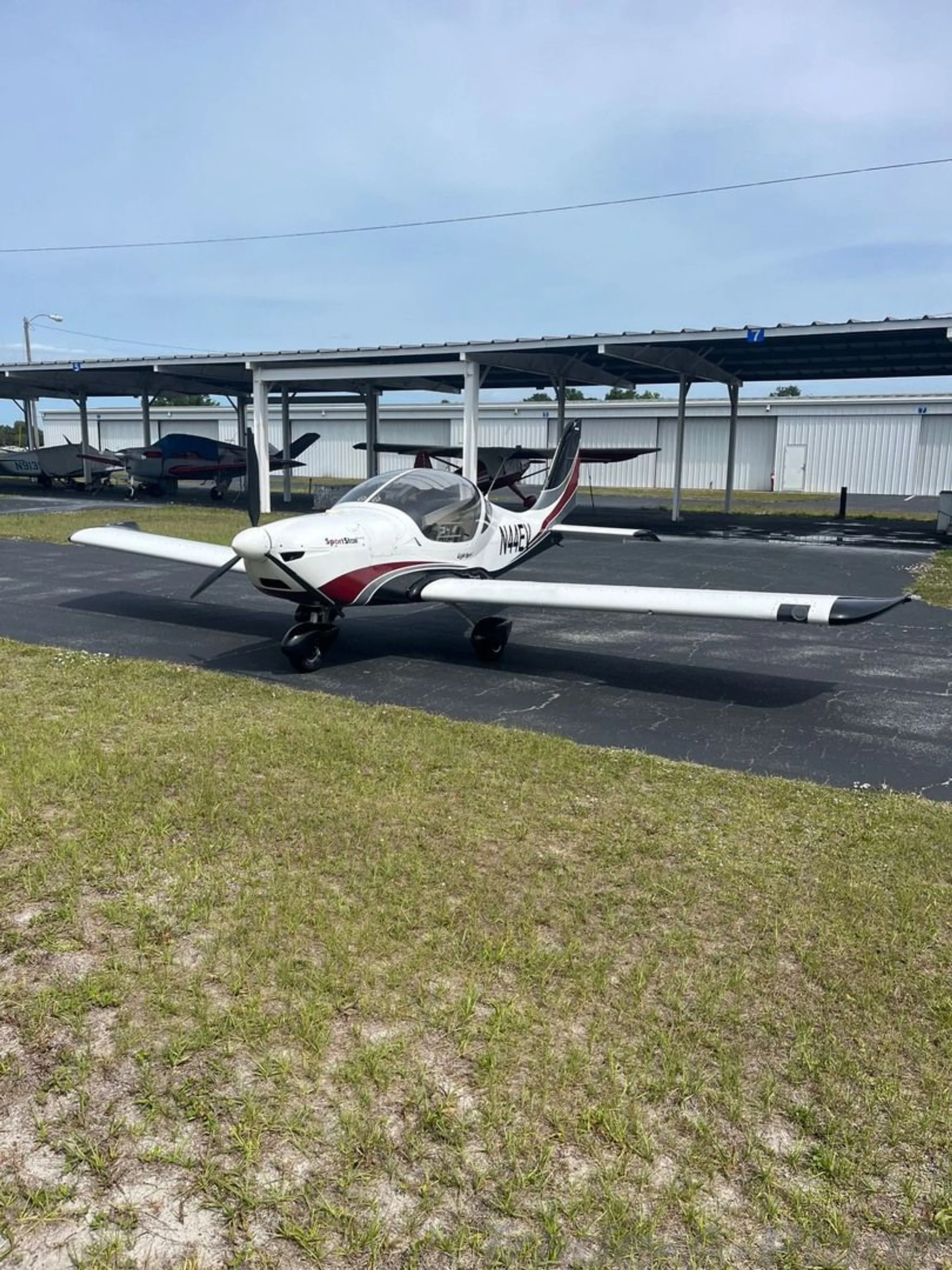 A white and red Evektor SportStar aircraft, tail number N44EV, is parked on an asphalt ramp next to hangars.