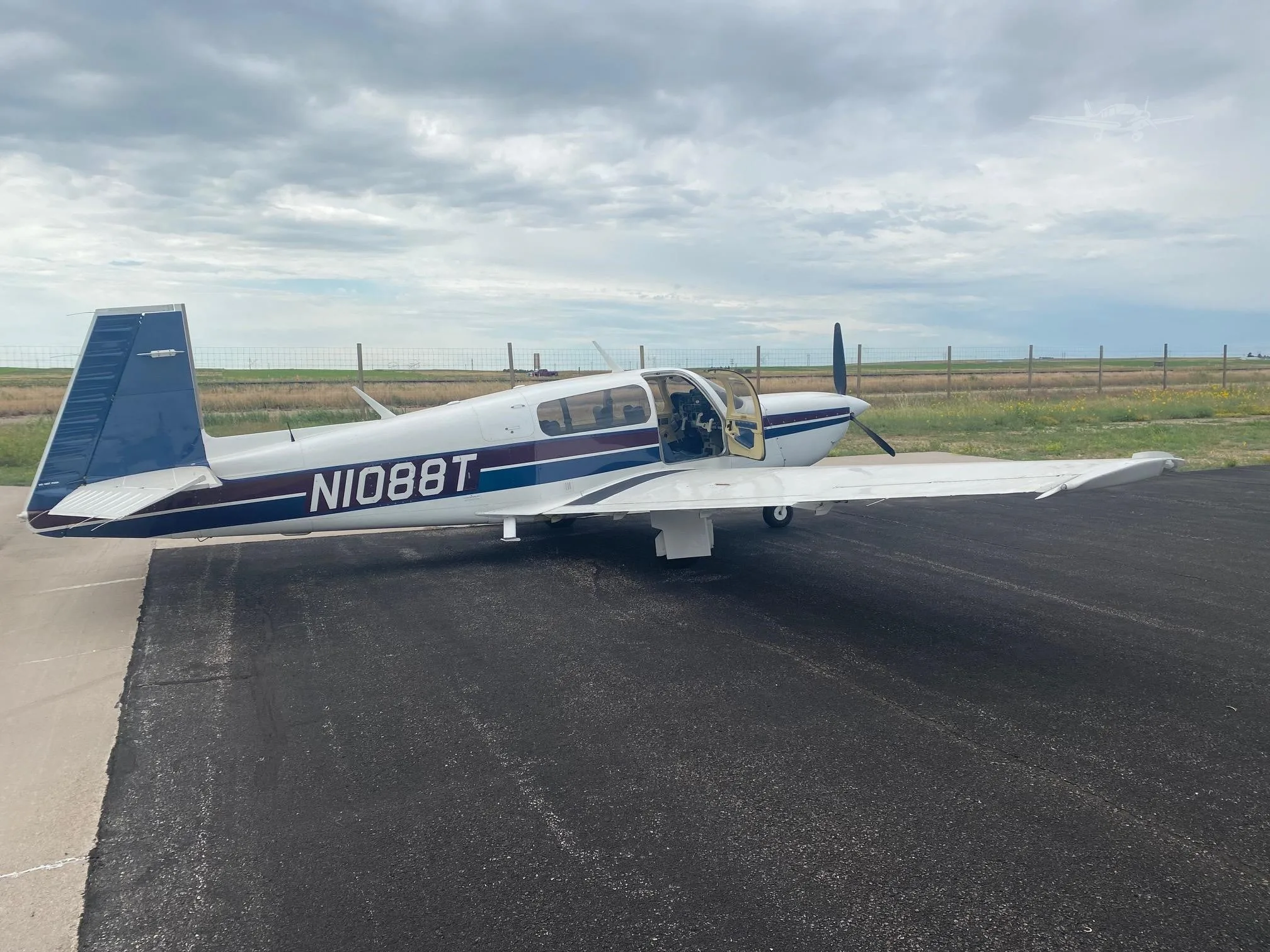 A white single-engine propeller aircraft with blue and maroon stripes, registration N1088T, parked on an asphalt ramp with its door open.