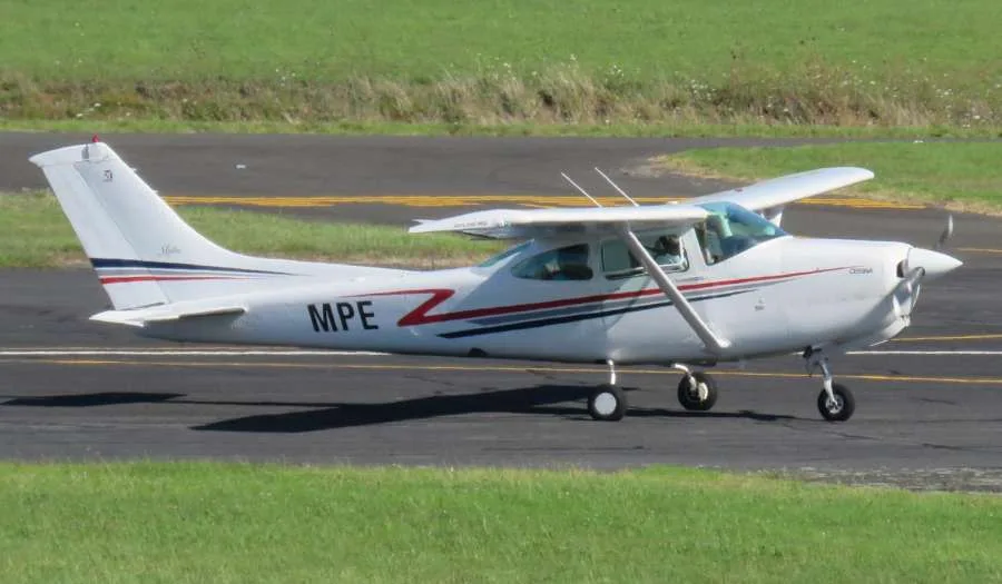A white Cessna aircraft with red and blue stripes and 'MPE' on the tail, taxiing on a runway.