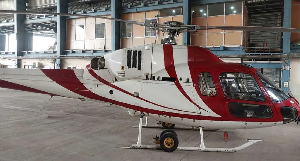 A close-up side view of a red and white helicopter with a striped paint scheme parked inside a hangar.