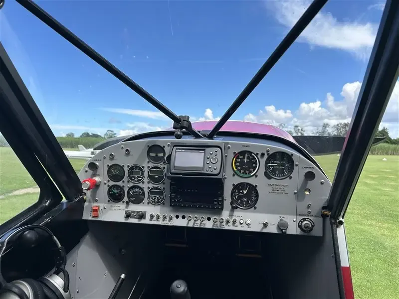 The cockpit instrument panel of the Super Cub, showing various gauges, a GPS unit, and radios, with the runway visible through the windshield.