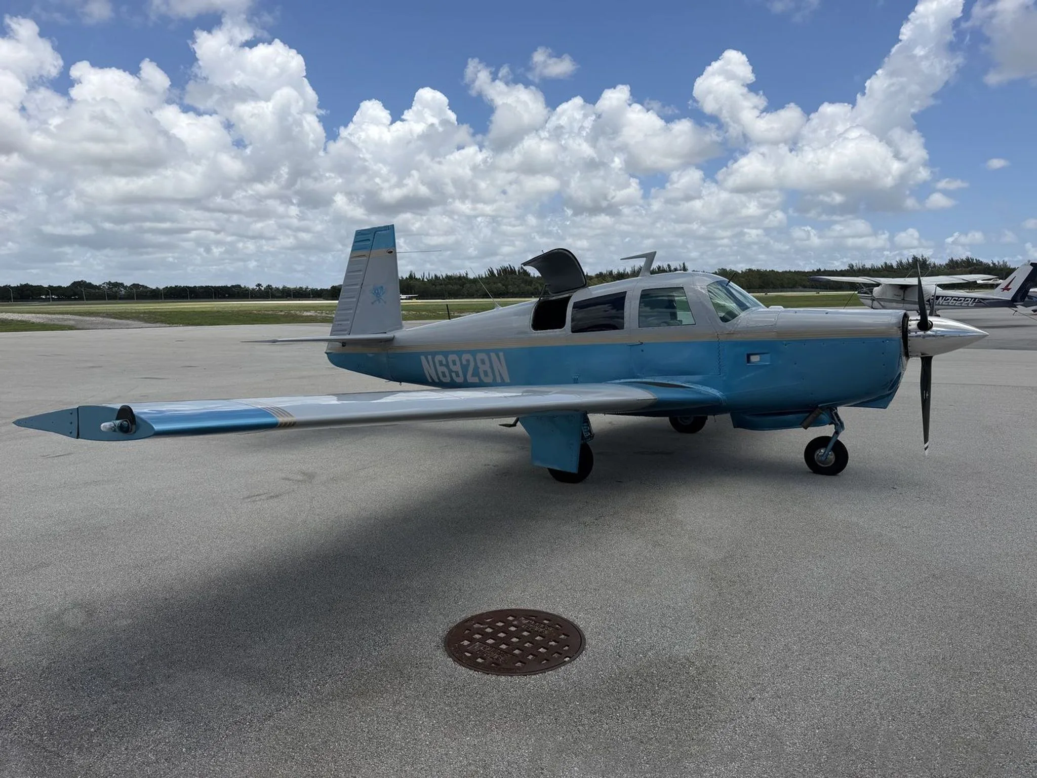 A light blue and white single-engine aircraft, N6928N, with its door open, parked on an airport tarmac.