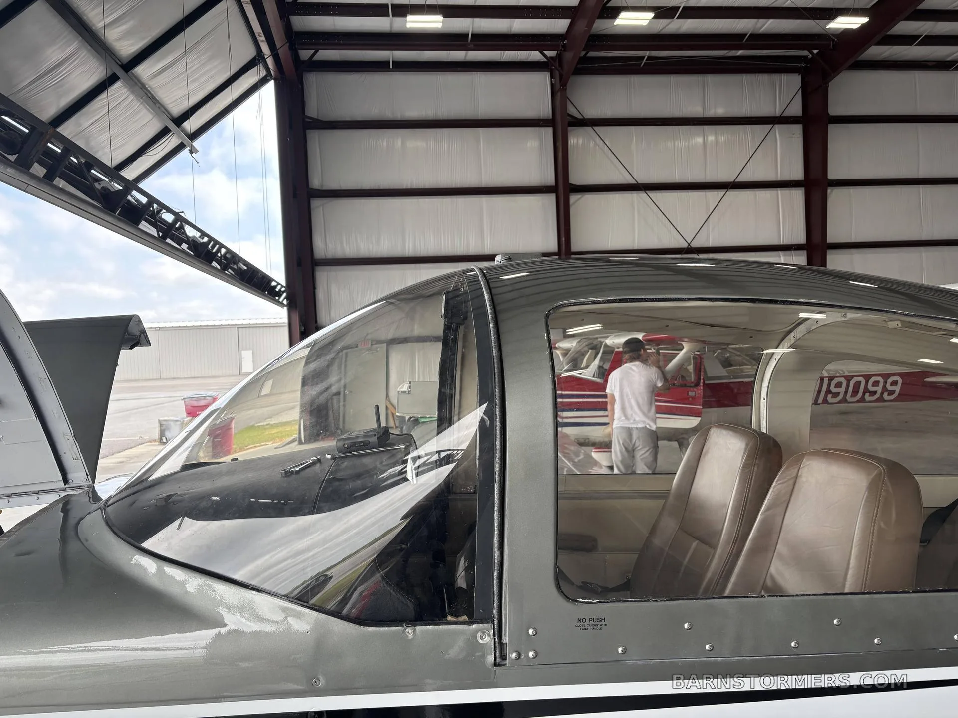 The brown leather seats of a Grumman American aircraft cabin, viewed from outside through the canopy, with another aircraft visible in the background.