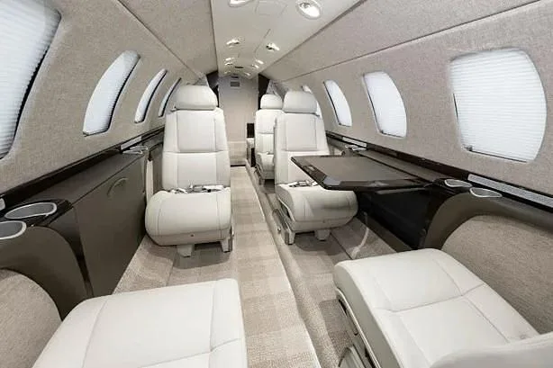 The aircraft's interior cabin with light-colored seats and a fold-out table extended.