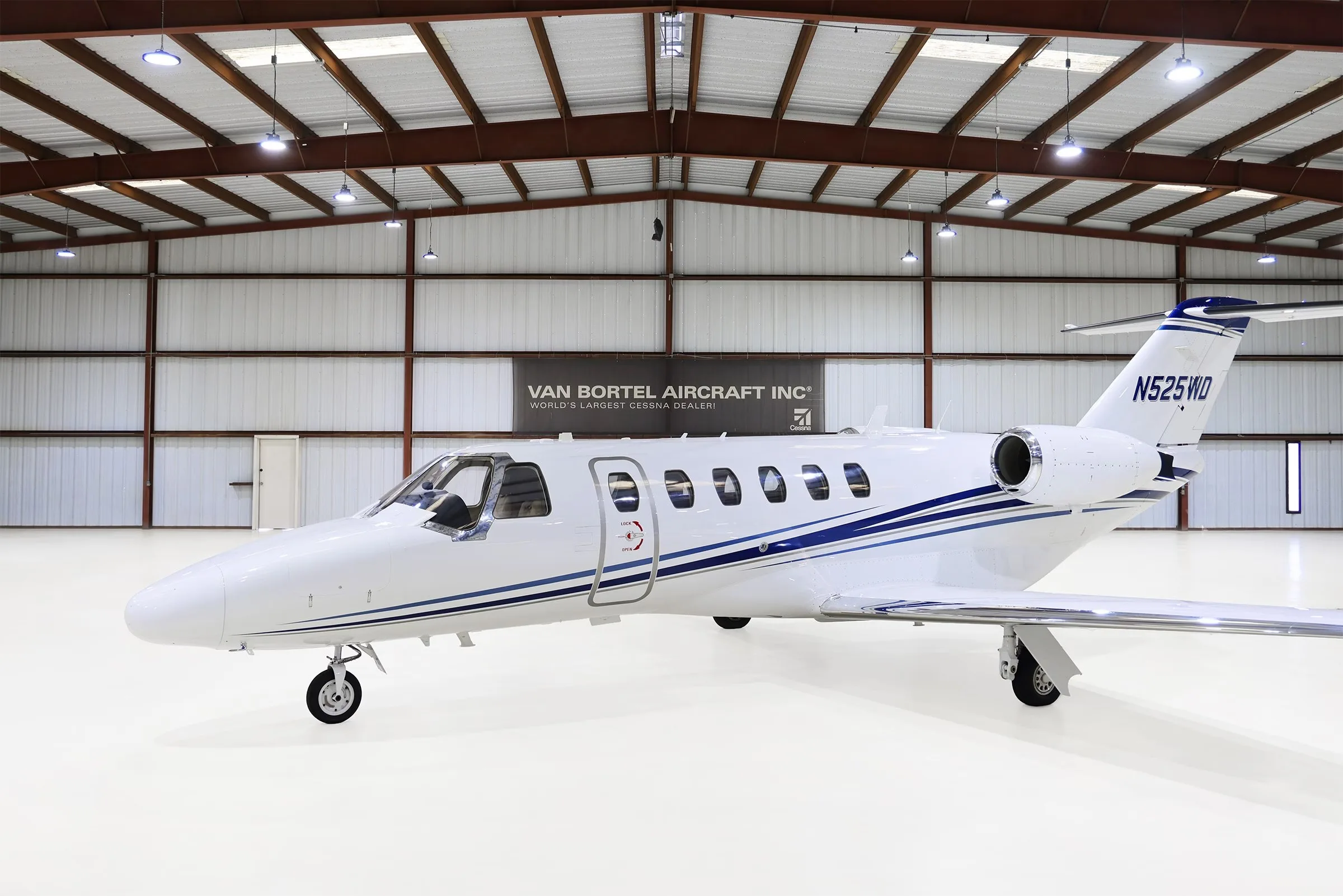 A white Cessna Citation CJ2+ (N525WD) with blue stripes parked in a hangar, viewed from the front-left.
