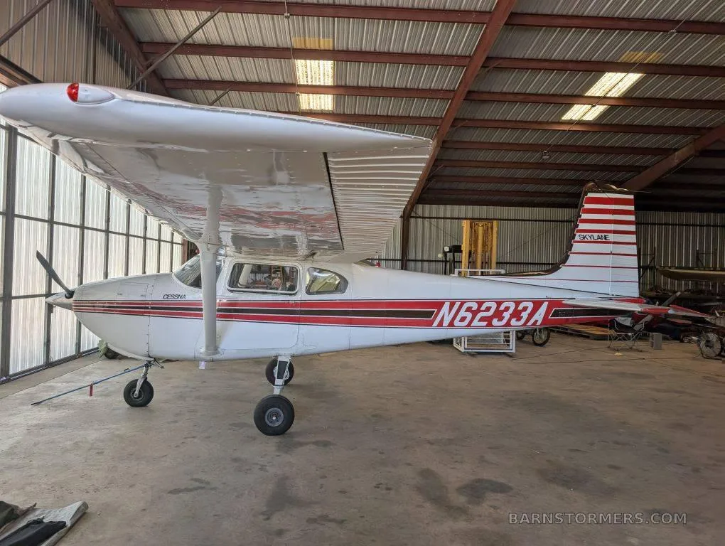 A white and red Cessna 182 Skylane (N6233A) with a red stripe paint scheme parked inside a hangar, viewed from the front-left.