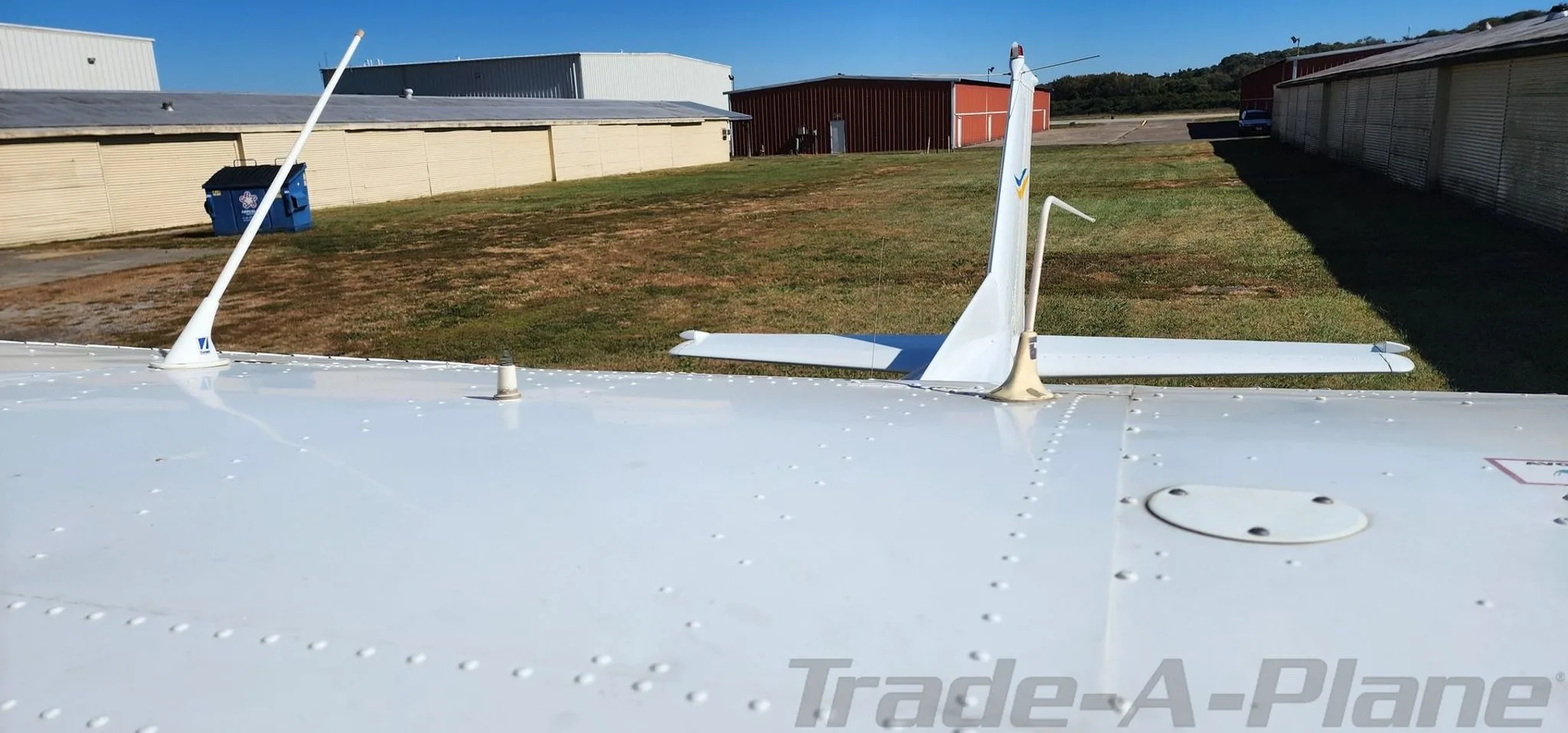 A close-up view of the white aircraft's top fuselage and tail, showing antennas and rivets against a background of hangars.