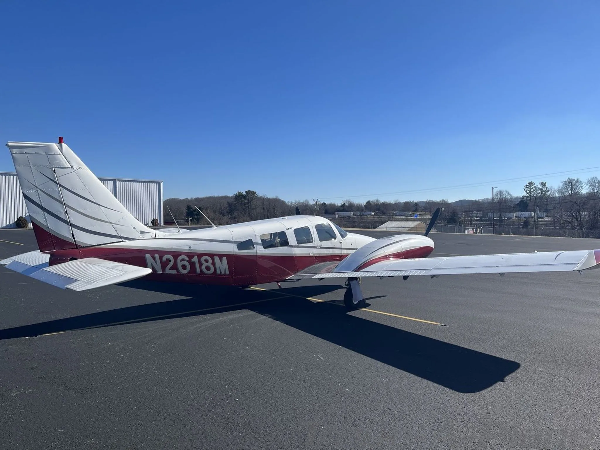 A side view of a white and maroon Piper N2618M twin-engine aircraft parked on an airfield, showing the registration number clearly.