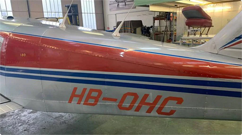 Close-up of the fuselage of a red and silver aircraft with blue stripes, showing the registration HB-OHC.