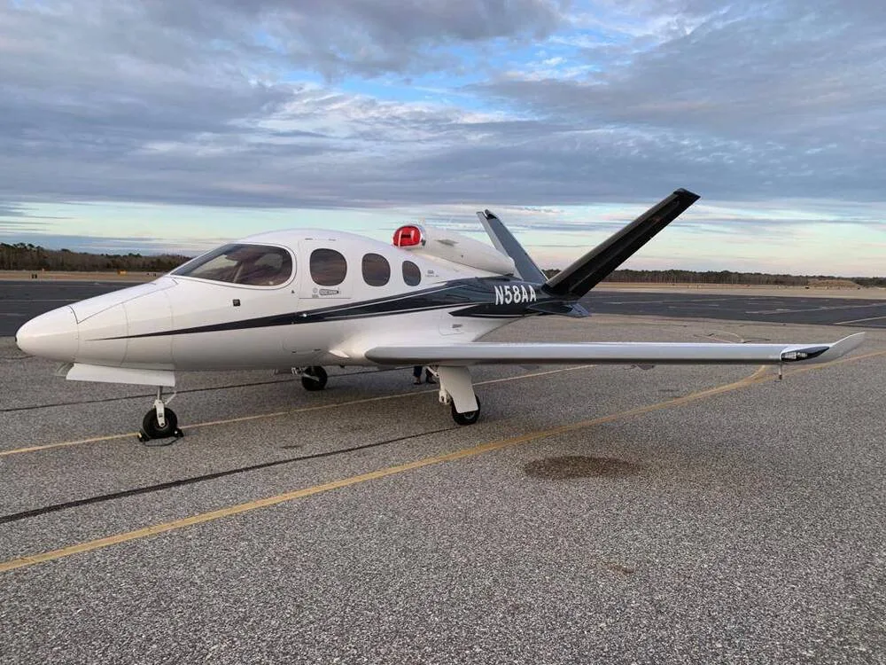 A white Cirrus Vision Jet with black and grey accents, registration N58AA, parked on an airport tarmac at dusk.