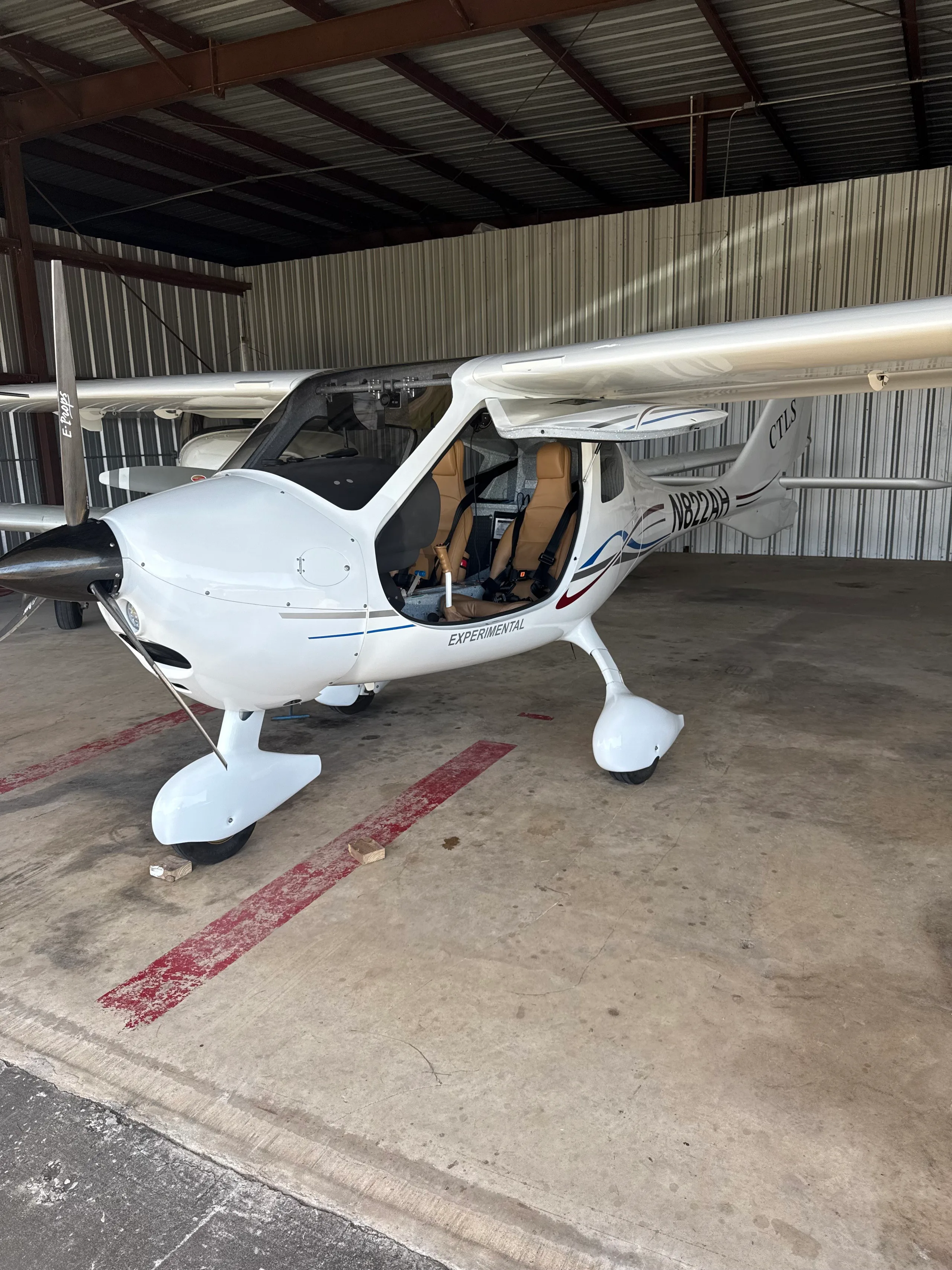 A white Flight Design CTLS light sport aircraft, registration N822AH, with its doors open, parked inside a hangar.