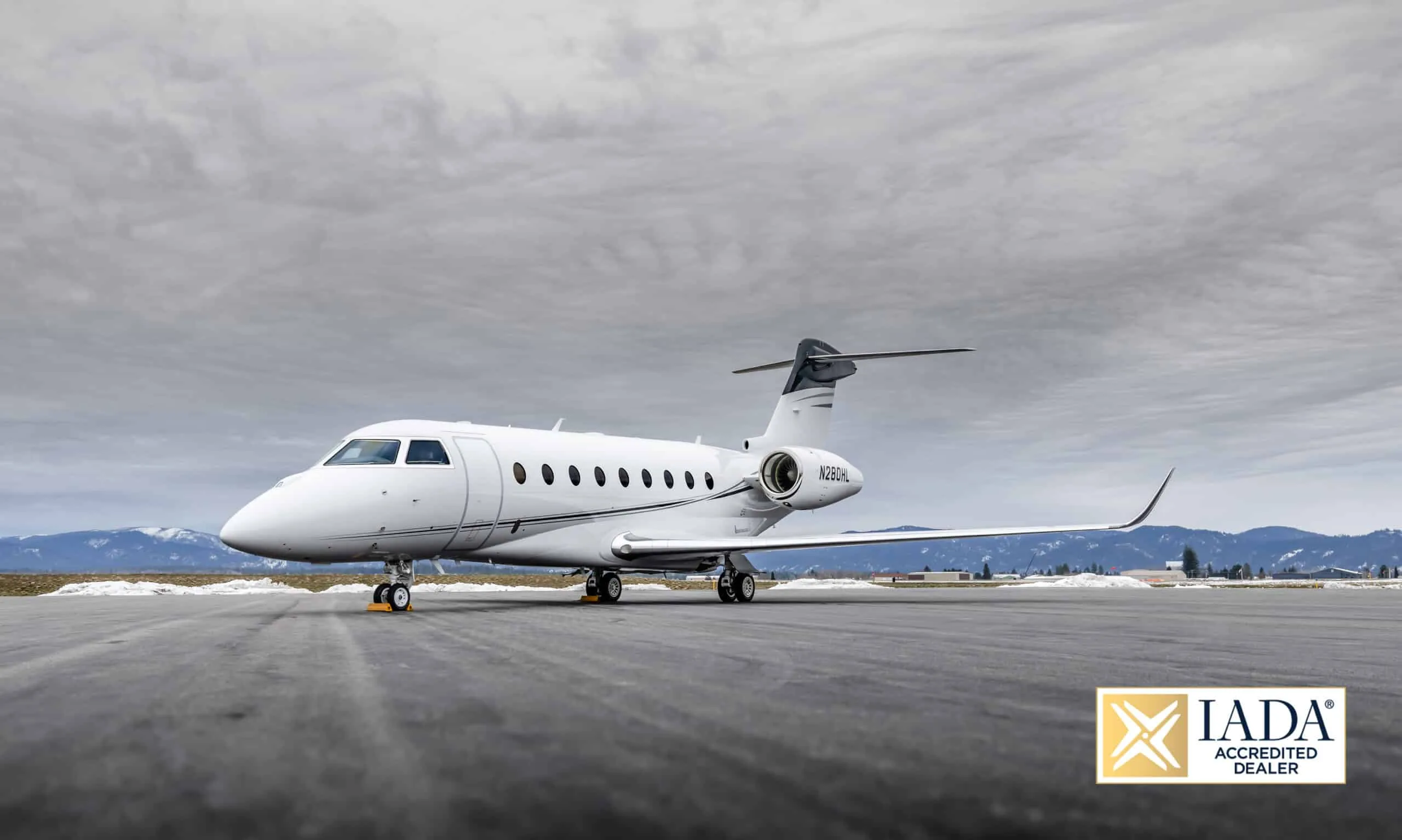 A white Gulfstream G550 (or similar large business jet) with registration N280HL parked on a snowy tarmac under a cloudy sky.