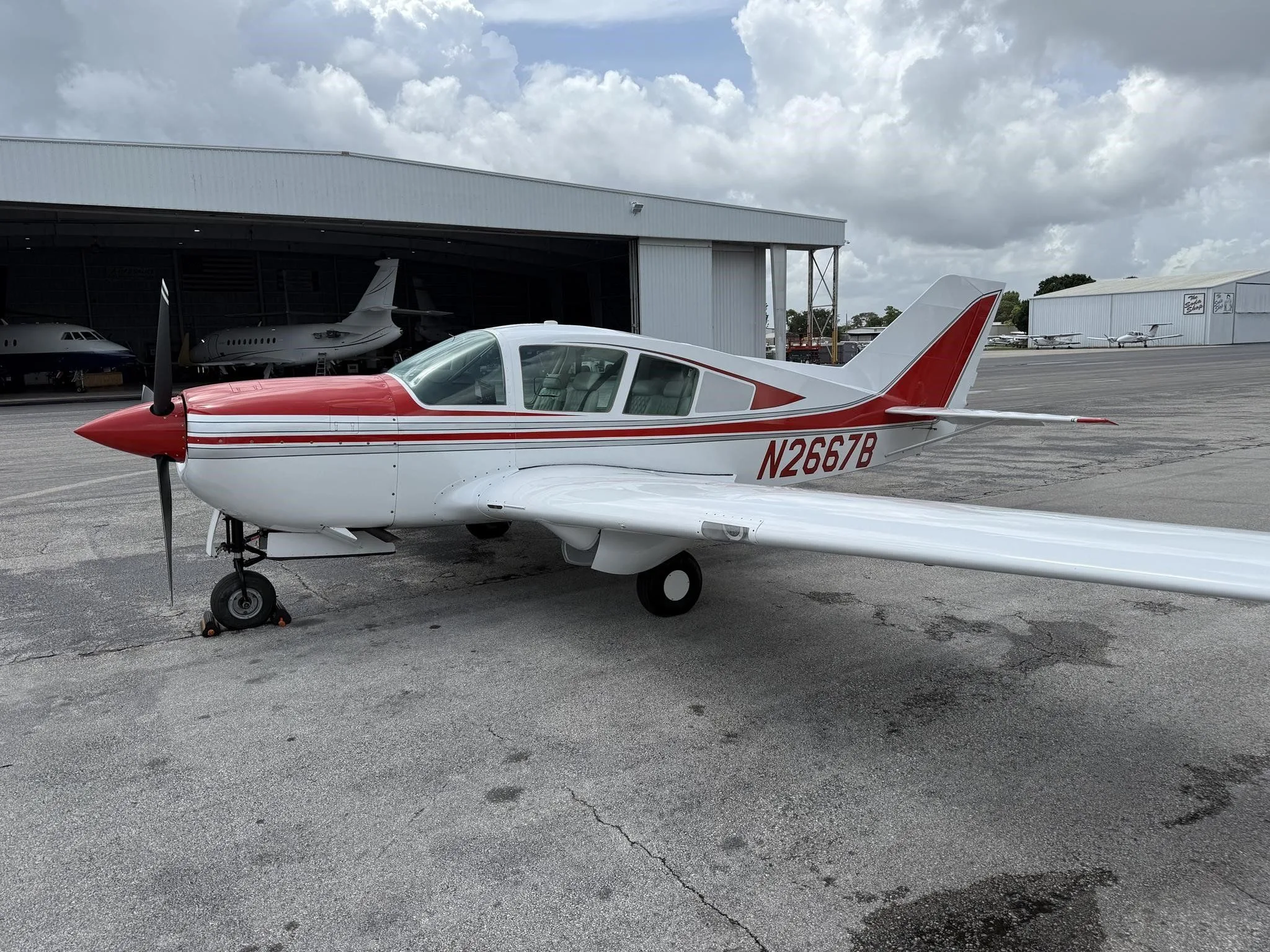 A white and red single-engine aircraft, N2667B, parked on an airport tarmac with hangars in the background.