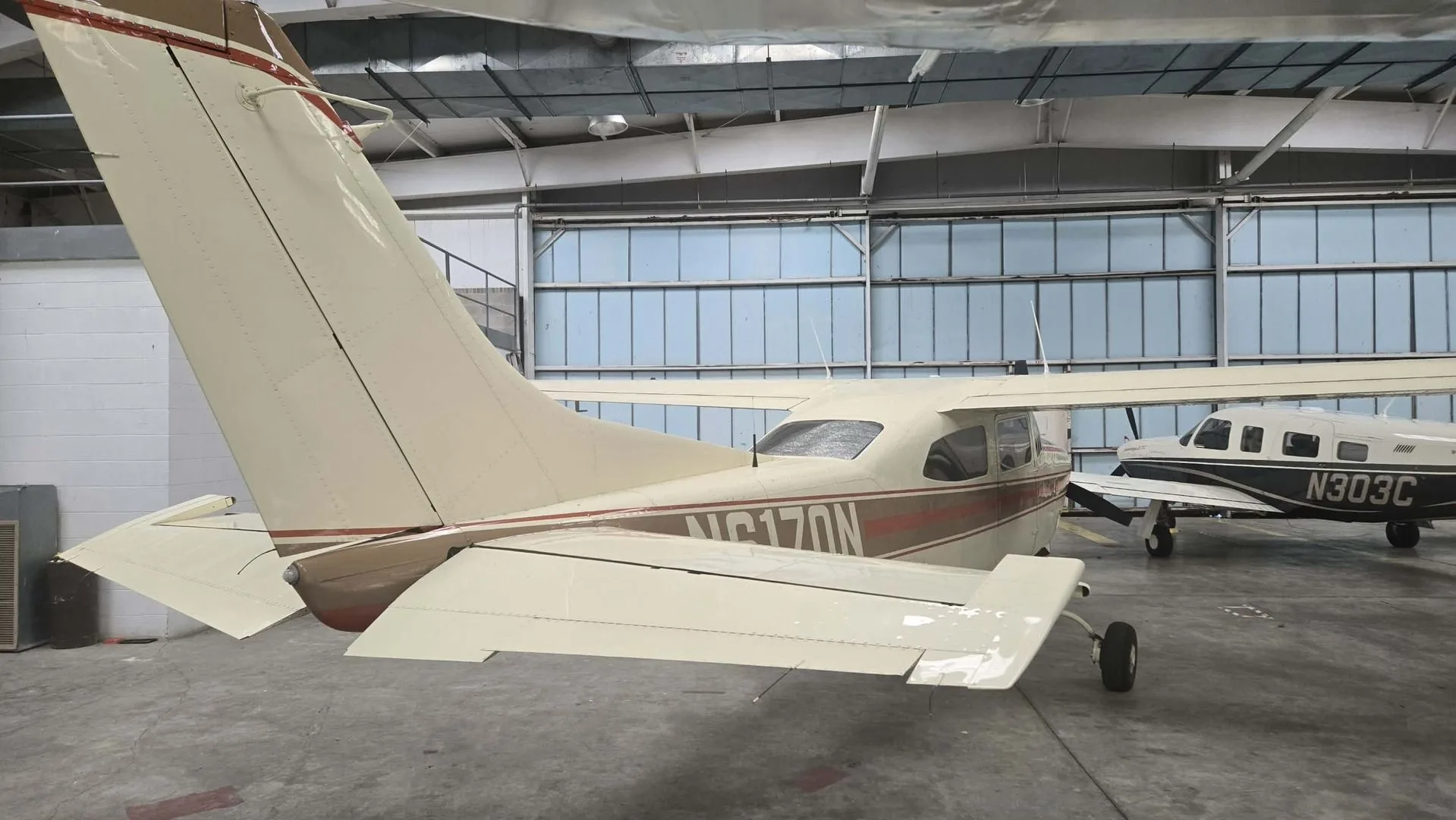 A rear-side view of the N6170N aircraft, showing its tail and wing, parked in a hangar next to another aircraft.