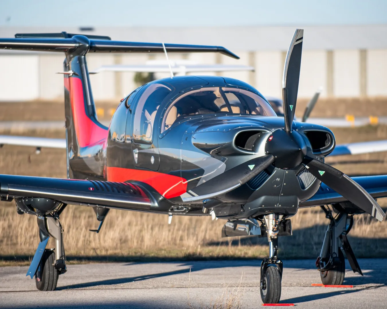 A dark grey single-engine propeller aircraft with red and white accents on an airfield, viewed from the front-right.
