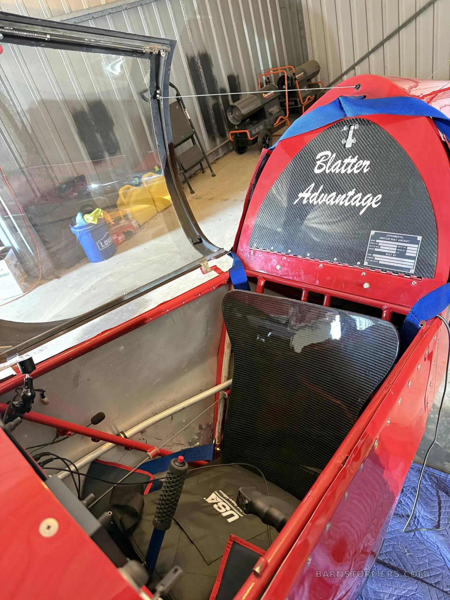 The open cockpit of a red aircraft, showing a single carbon fiber seat and the "Blatter Advantage" name on the headrest.