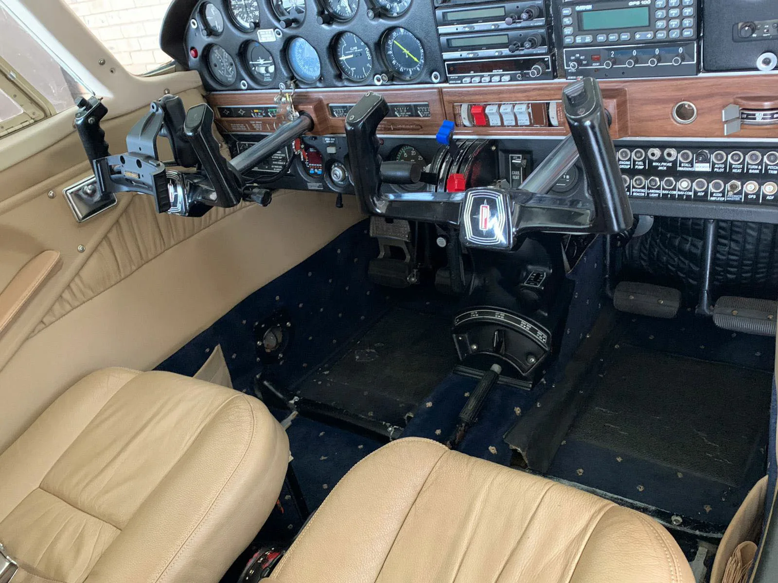 The cockpit of a light aircraft with dual yokes, a complex instrument panel, and tan leather seats.