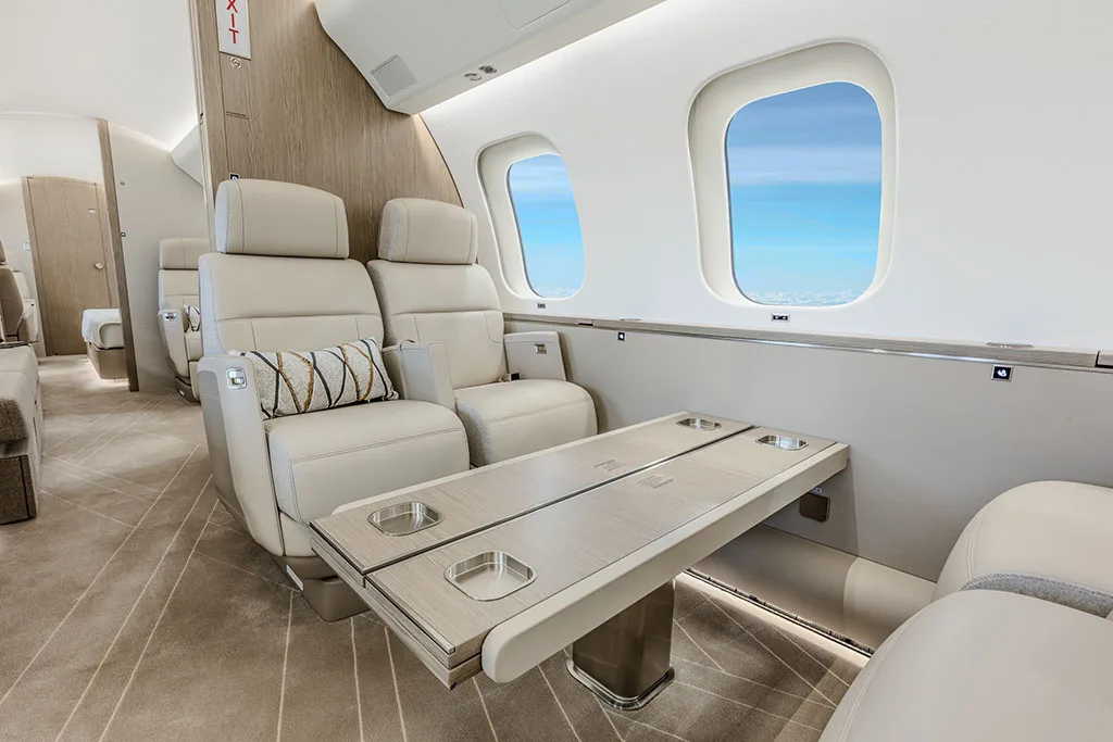 Close-up view of two beige leather seats and a large fold-out table in a private jet cabin.