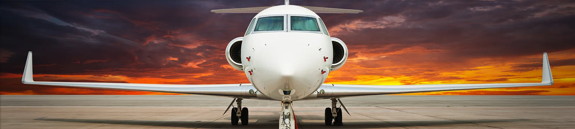 Front view of a private jet against a dramatic sunset sky.