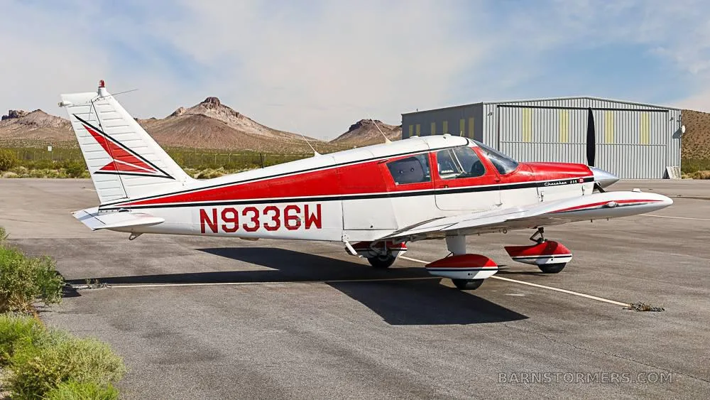 Side view of a red and white Piper Cherokee 235B (N9336W) parked on an airfield next to a hangar.