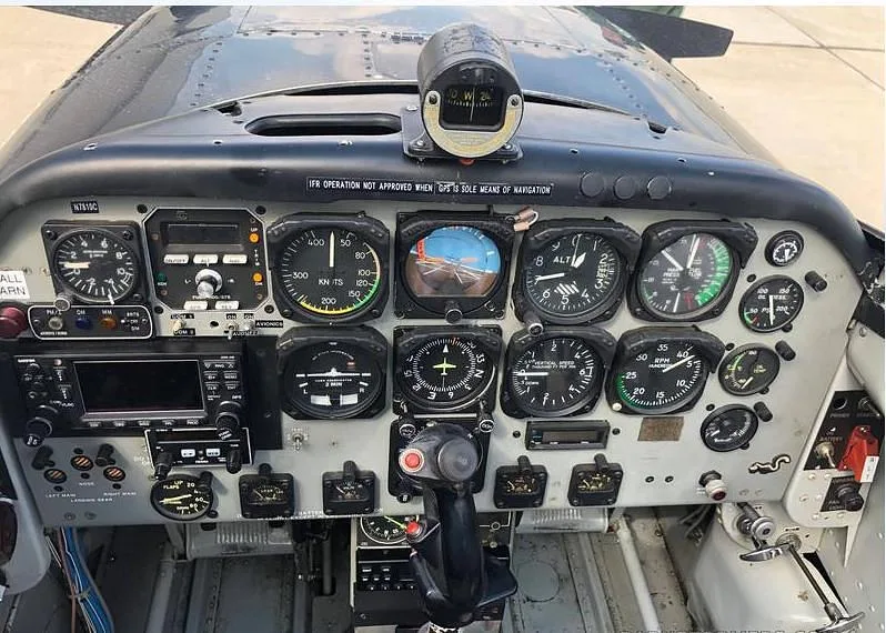 The detailed instrument panel of an aircraft, featuring various analog gauges, a compass, and a small digital display.