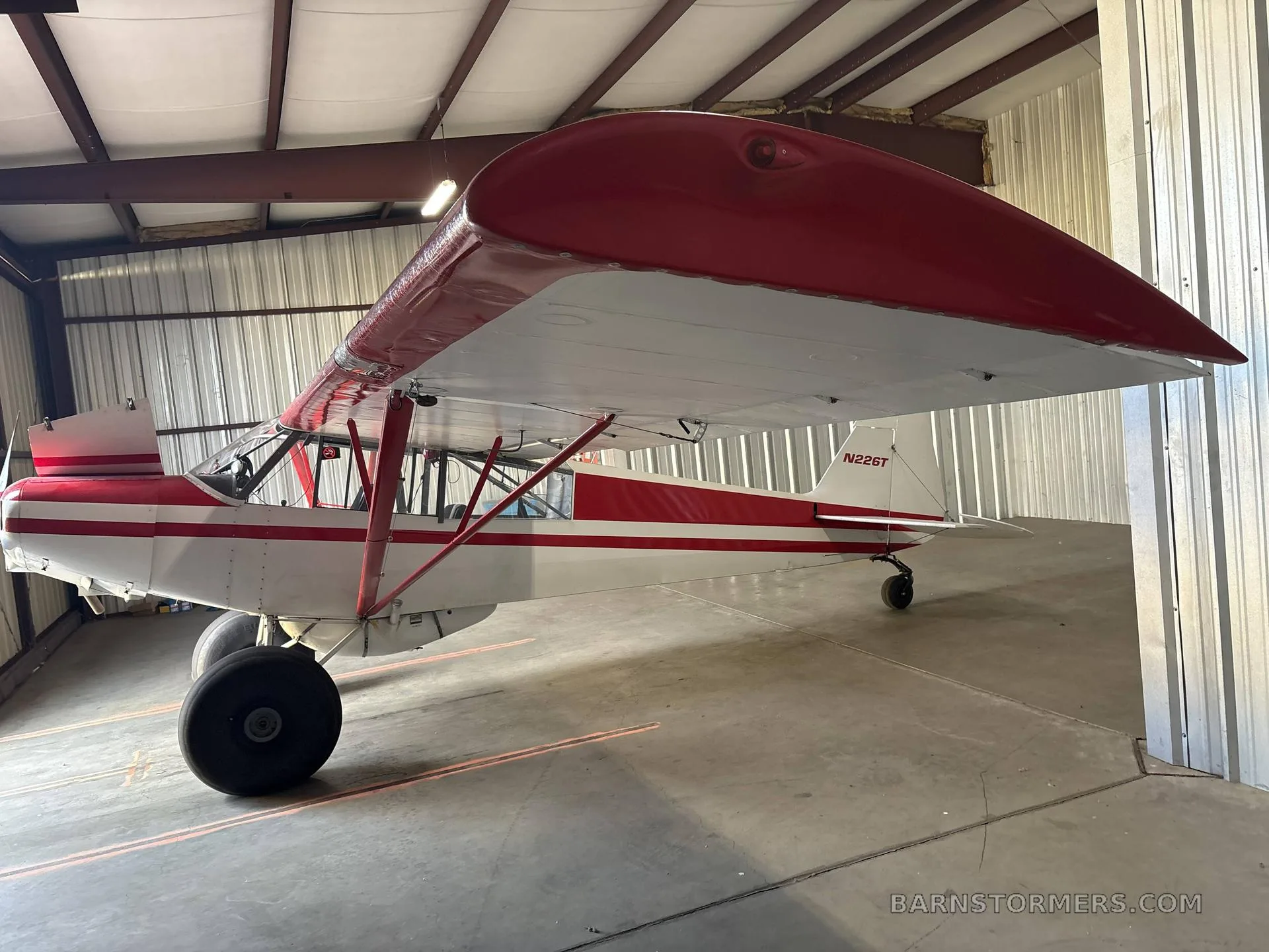 A red and white bush plane with large tires, tail number N226T, parked inside a metal hangar.