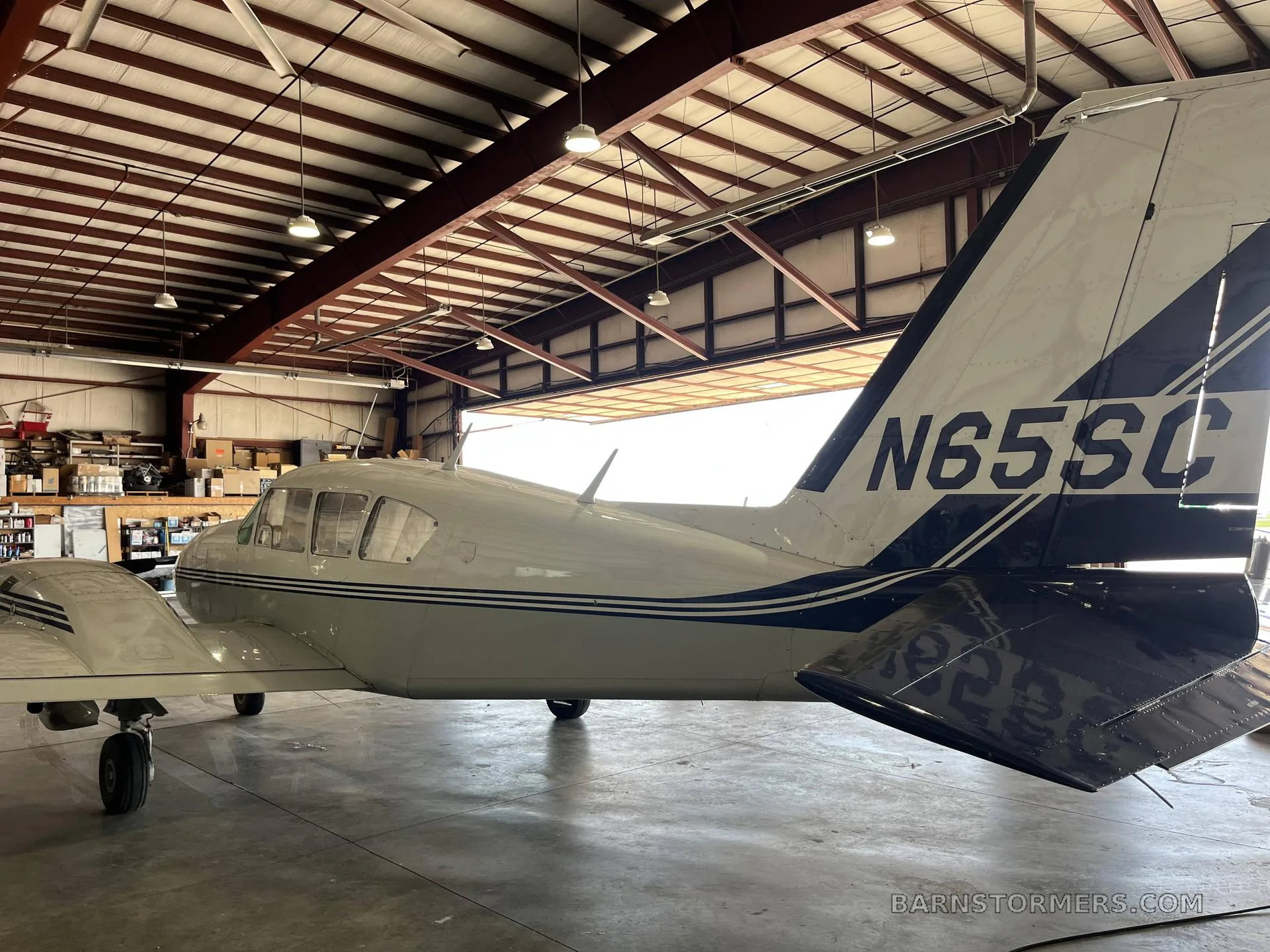The tail section of a white twin-engine aircraft with blue stripes (N65SC) parked in a hangar.