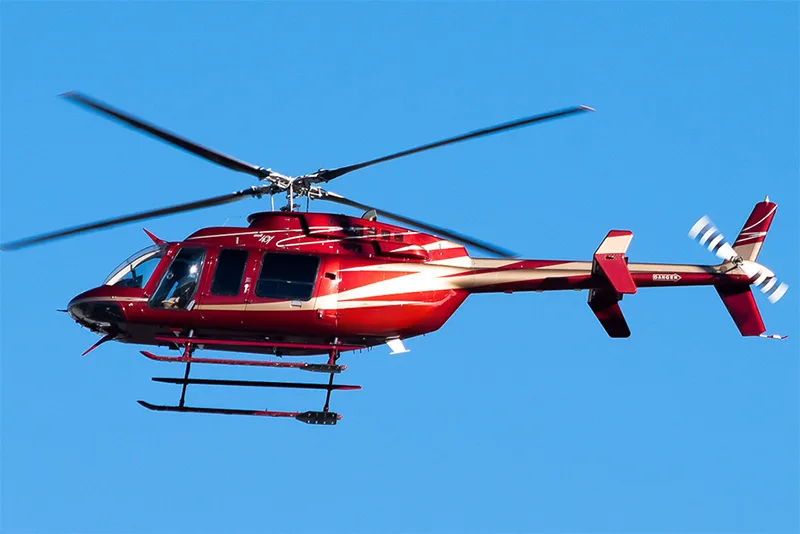 A red helicopter with white and gold stripes flies against a clear blue sky.