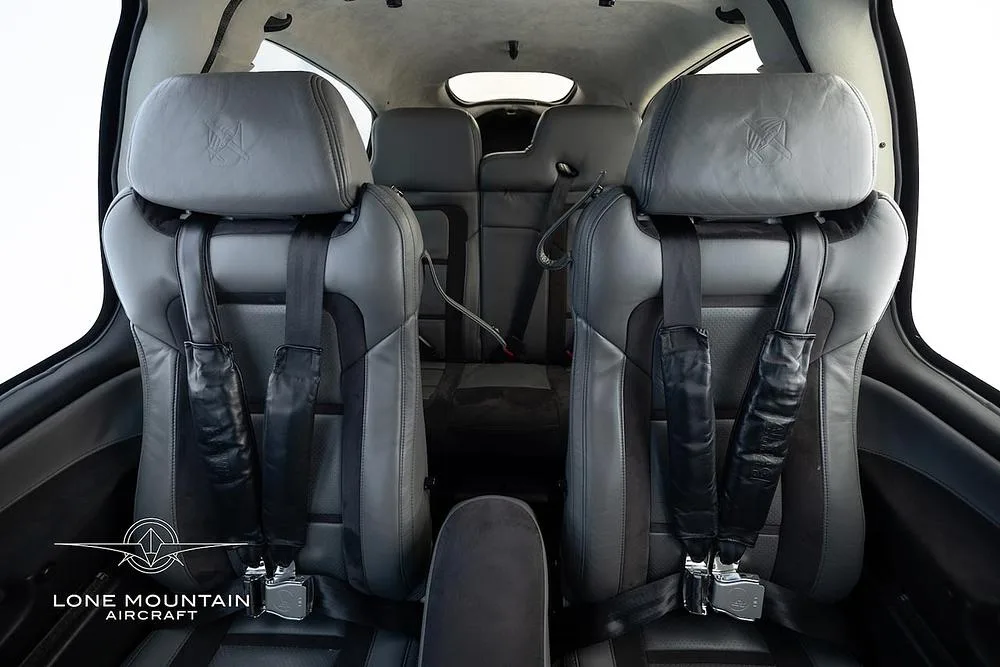 The grey leather front seats of an aircraft cabin, with seatbelts fastened.
