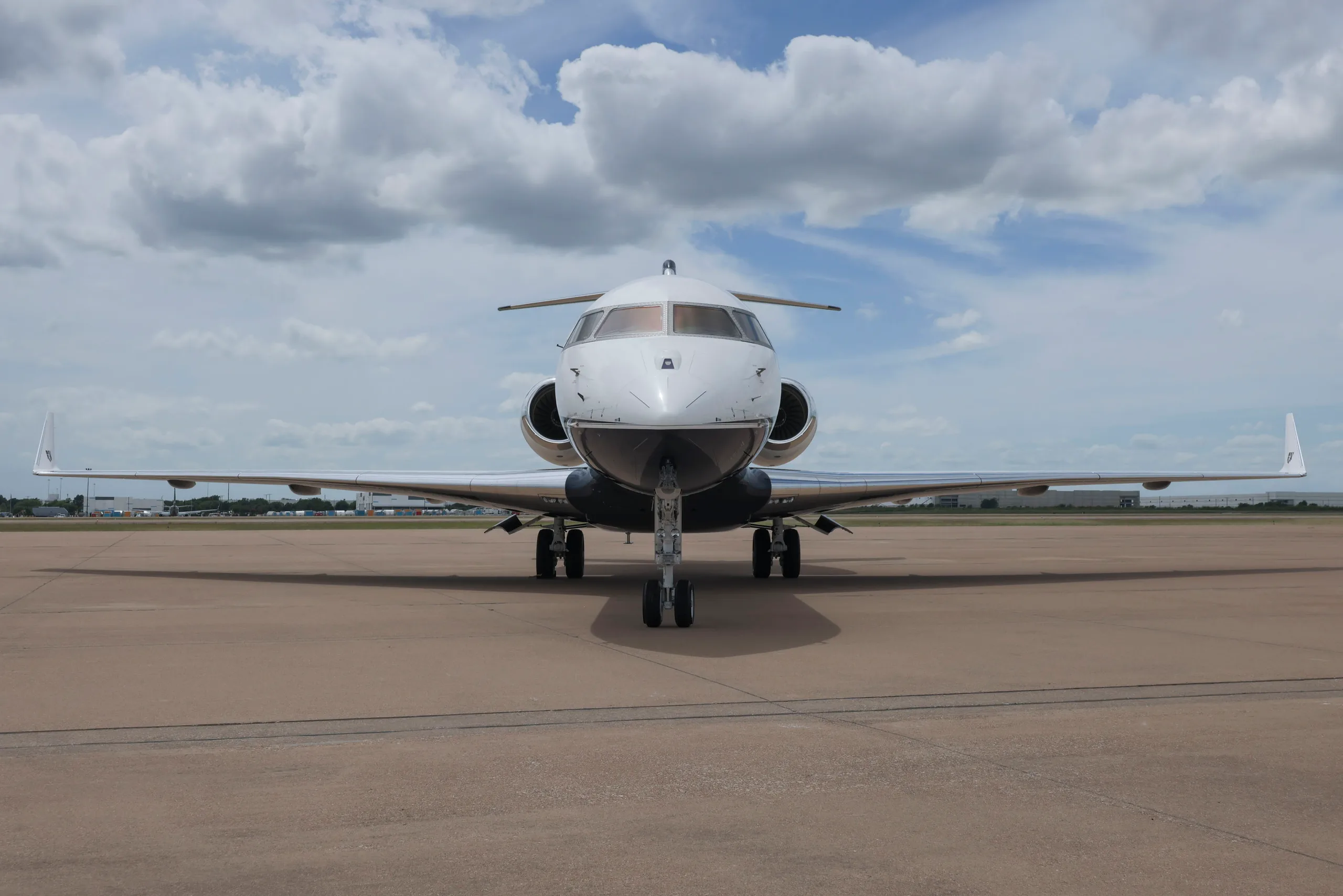 A head-on view of a white and dark blue Bombardier Global Express business jet parked on an airfield.