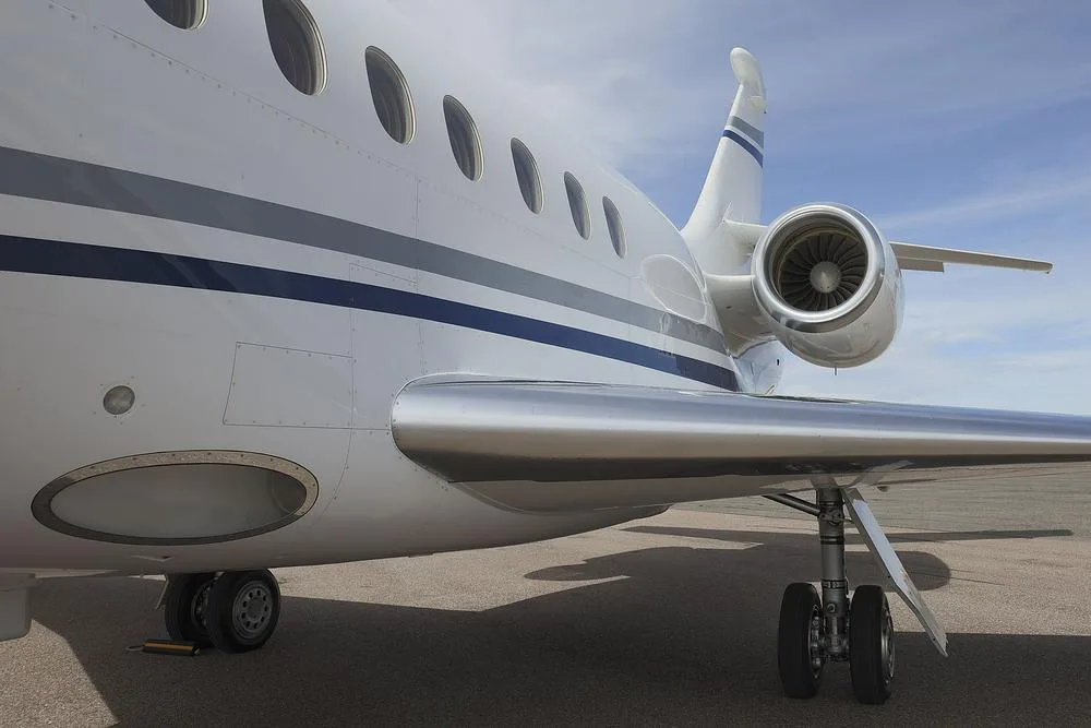 A close-up view of the fuselage, wing, and engine of a white Dassault Falcon 900 business jet.