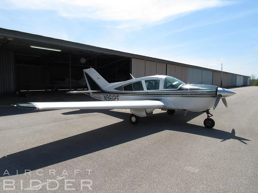 A front-side view of the white and dark green single-engine aircraft N9612E parked on a tarmac in front of an open hangar.
